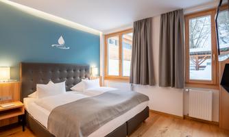 A modern room with a double bed and bright color accents. Large windows provide plenty of daylight and a pleasant atmosphere.