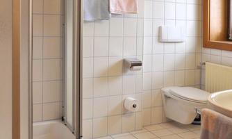 A modern bathroom with shower and toilet. The walls are tiled, and some towels are hanging.