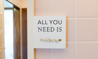 A sign with the inscription "ALL YOU NEED IS LOVE" on a wall. The background is in soft shades of pink.