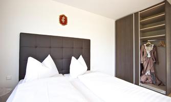 A modern bedroom with two beds and white bedding. In the background, there is a wardrobe with a dress visible.