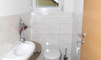 A modern bathroom with a toilet and a small sink. There is a window that lets in daylight, and bright tiles on the walls.