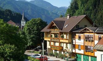 A picturesque mountain landscape with traditional houses and lush greenery. In the background, mountains and a church tower can be seen.