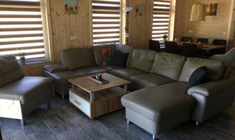 A modern living room with a comfortable, bright sofa and a square coffee table. The walls are made of wood and large windows provide plenty of natural light.