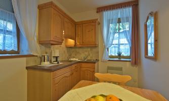 A cozy kitchen with wooden furniture and large windows. On the table, there is a bowl of fresh apples and oranges.