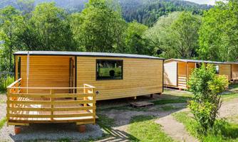 A series of modern wooden holiday homes in a green environment. Gentle hills are visible in the background.