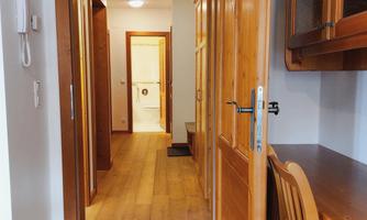 A bright hallway with wooden flooring and open doors to various rooms. On the left side, there is a table with chairs.