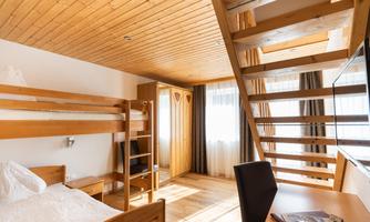 A bright room with wooden furniture and large windows. It contains a bunk bed and a staircase to an upper area.