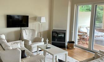 A bright living room with comfortable white sofas and a modern television. Large windows provide a view of a balcony with seating options.
