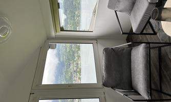 A comfortable living area with two chairs, large windows, and a view of a lake. The view shows a green landscape and a cloudy sky.