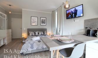 A modern room with a cozy bed and a table. A television hangs on the wall, and there are decorative elements and a bright atmosphere.