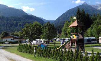 A cozy campsite with a playground and caravans nestled in a picturesque mountain landscape. The surroundings are green and inviting, perfect for families.