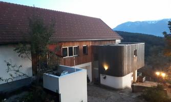 A modern house at dusk, surrounded by trees and mountains. The architecture combines wood with white walls, creating a contemporary look.