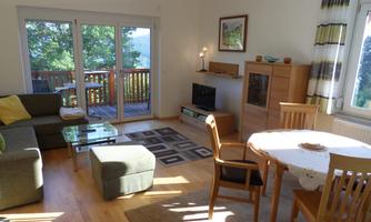 Bright apartment with a cozy living room and dining table. Large windows offer a view of the greenery.