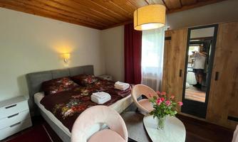 A cozy bedroom with a double bed and floral bedding. The furnishings include a small table with vases and a large wardrobe.