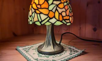 A decorative table lamp with a lampshade made of colorful glass that features floral patterns. It stands on a lace-covered base.