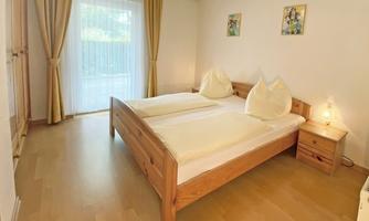 A bright bedroom with a double bed and cozy wooden decor. Large windows let in plenty of daylight and give the room a friendly atmosphere.