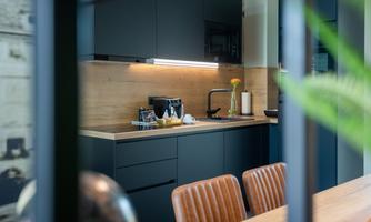 Modern kitchen with dark blue furniture and light wooden elements. In the foreground, elegant chairs can be seen.