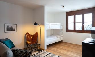 A modern room with a loft bed and a cozy seating area.  
Large windows provide plenty of daylight and a welcoming atmosphere.
