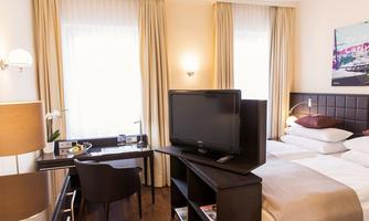 A comfortable hotel room with a double bed, a television, and a desk. Large windows ensure plenty of daylight and an inviting atmosphere.