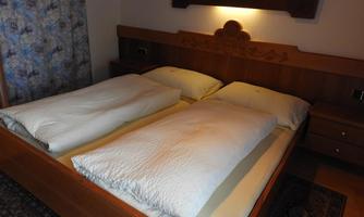 A cozy bedroom with a double bed and two separate blankets. The walls are painted in light colors, and there is a small bedside table next to the bed.
