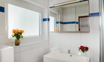 A modern bathroom with white tiles and blue accents. There is a sink area with flowers and a large mirror.