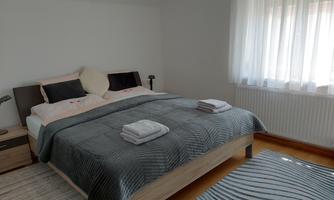 A cozy bedroom with a double bed and fresh towels. The walls are light, and large windows let in a lot of light.