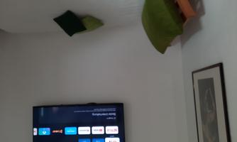 A cozy room with a single bed and a TV on the wall. There are two green pillows on the bed.