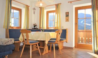 A bright dining room with a round table and chairs. Large windows provide plenty of daylight and a view of the mountains.