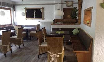 A cozy restaurant with wooden furniture and an inviting atmosphere. There are table settings and a small plant decoration on the wall.