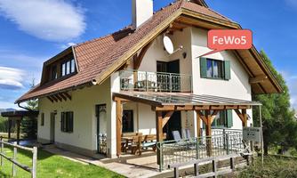 A charming holiday home with a large garden and a visible balcony. The facade is bright and inviting, surrounded by a beautiful landscape.
