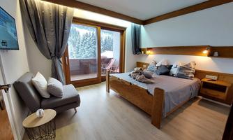 A cozy bedroom with a large bed and a balcony. The view shows snow-covered trees and a relaxing atmosphere.