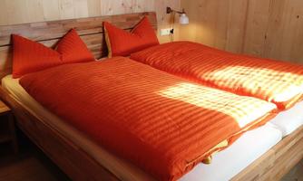 A cozy bedroom with a double bed and orange bedcovers. The walls are made of light wood and the lighting creates a warm atmosphere.