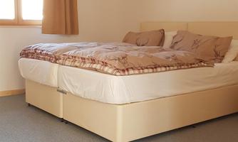 A bright bedroom with a large bed and a window. The walls are neutral, and the floor is carpeted.