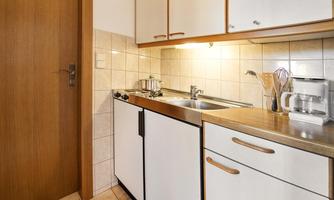A small kitchen with white cabinets and a sink. The walls are tiled with light tiles.