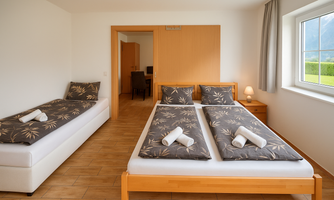 A cozy bedroom with two single beds and an extra bed. The room has large windows that let in plenty of natural light.