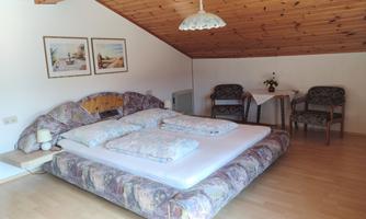 A cozy bedroom with a large bed and wooden ceiling. Two chairs and a table complete the furnishings.