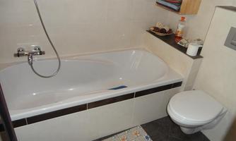 A modern bathroom with a bathtub and a toilet. The tiles are simple and light-colored.