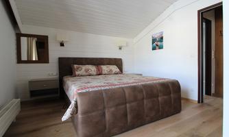 A cozy bedroom with a large bed and wooden floor. A picture hangs on the wall and there is a mirror next to the bed.