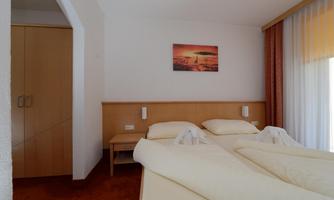 A cozy bedroom with two beds and soft colors. A picture of a sunset hangs on the wall.
