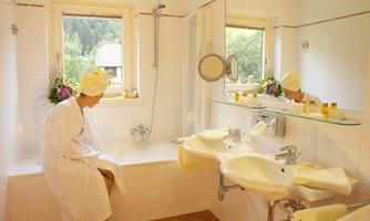 A modern bathroom with a bathtub and two sinks. A person in a bathrobe sits comfortably on the edge of the bathtub.