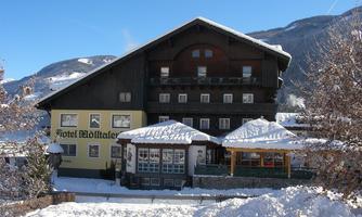 A charming hotel in the snow, surrounded by mountains. The facade is made of wood and the entrance has a covered area.