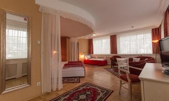A bright room with large windows and elegant furnishings. There is a bed, a cozy seating area, and a desk.