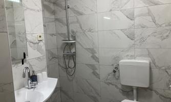 A modern bathroom with a marbled tiled floor. It includes a shower, a sink, and a toilet.