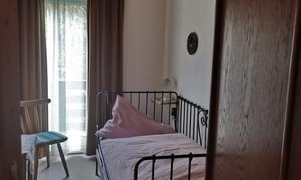 A simple room with a single bed and a chair. The window lets in a lot of light and the room has a cozy atmosphere.