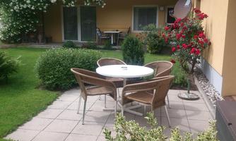 A cozy garden with a round table and chairs. Colorful flowers and well-maintained bushes create an inviting atmosphere.