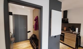 A modern hallway with a gray wall accent and a view of a stylish kitchen. The floor is made of wood, and there is a coat rack.