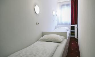 A simple room with two single beds and a window. The walls are white and there are red curtains.