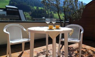 An inviting balcony with a round table and two plastic chairs. On the table are glasses and a few yellow mugs, surrounded by a beautiful mountain landscape.