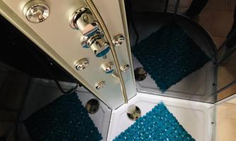 A modern shower cabin with shiny fixtures and a blue shower mat. The interior is bright and reflects on the walls.