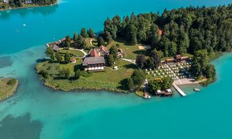 An idyllic island with green trees and clear blue water. Several buildings and sun loungers are located along the shore.